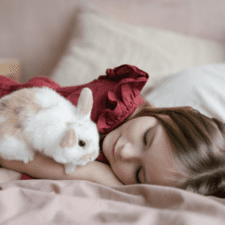 A girl in red laying on the bed with a brownish patch rabbit